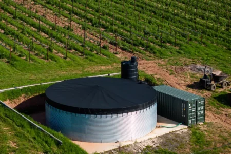 Large metal water storage tank with a black cover next to a green container